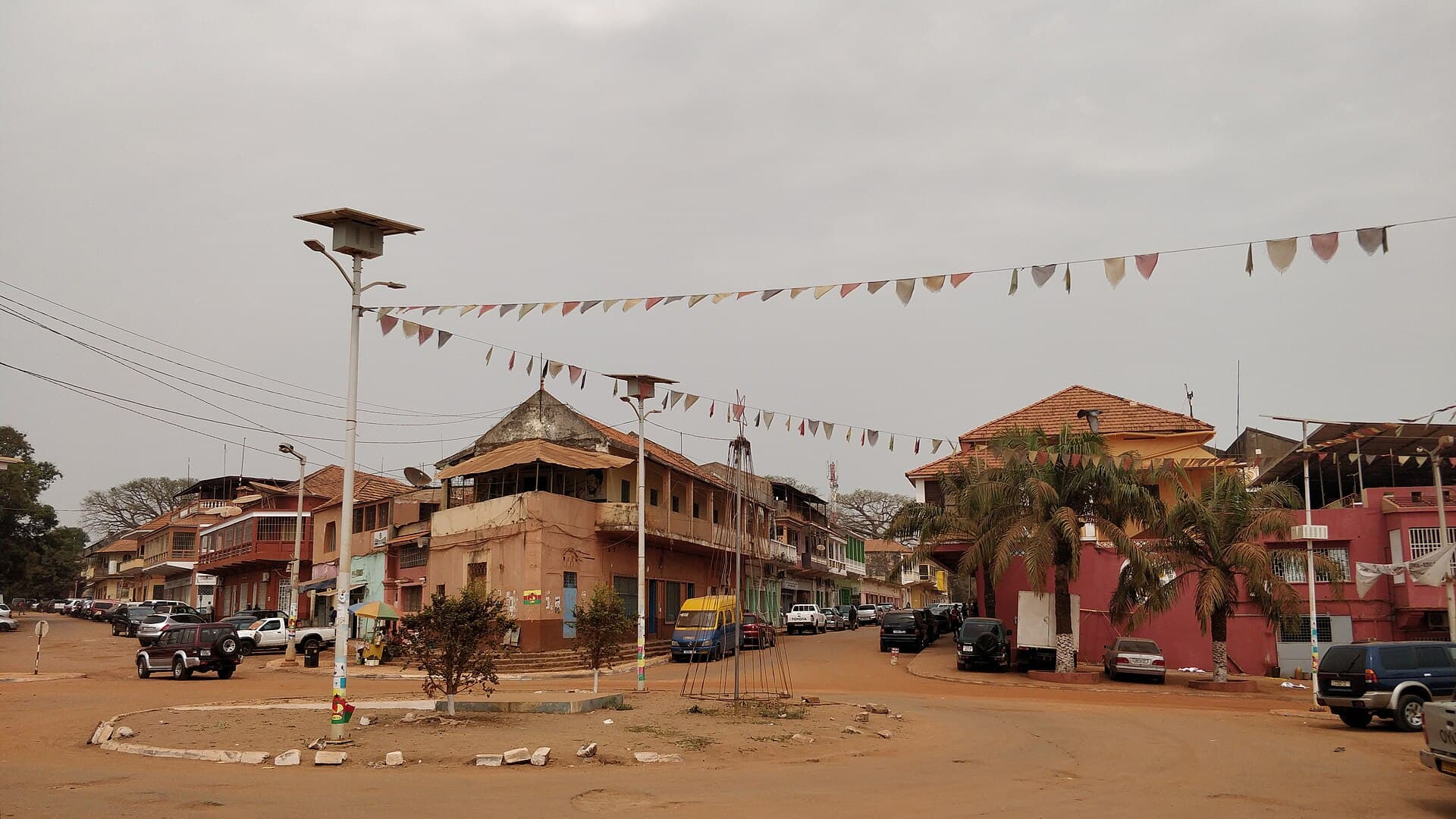 Uma praça de Bissau Velho com casario colonial, palmeiras e bandeirolas