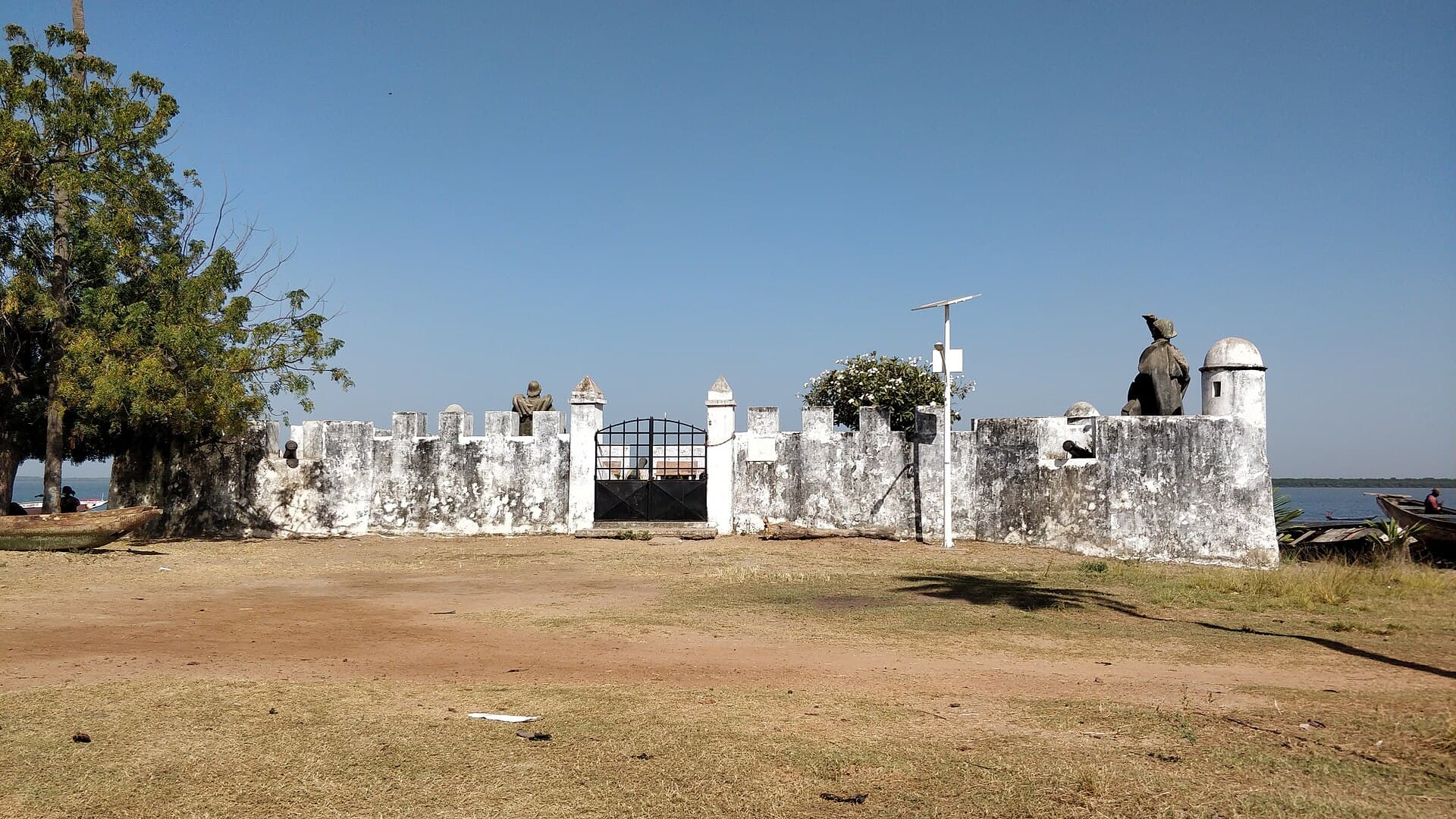 As muralhas brancas da fortaleza de Cacheu, com estátuas e o rio ao fundo